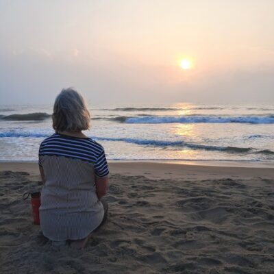 woman sitting on a beach at sunrise in quiet reflection