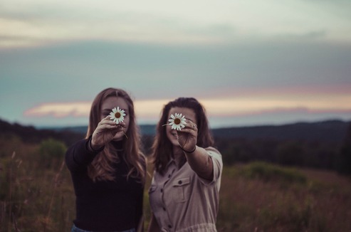 Two young women holding daises in outstretched arms at sunset in the present moment which will change into the future and their future personal story