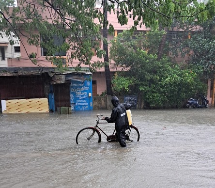 Person in rain gear pushing a bike through a flooded street struggling to accept the circumstances
