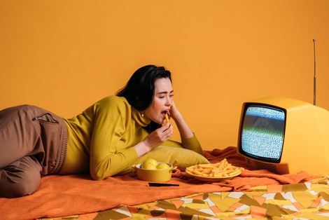 women eating food while laying down binge watching TV mindlessly