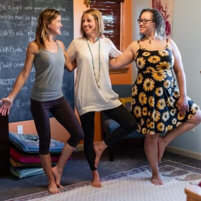 Author with two other women supporting each other in tree pose with arms around each other and smiling together
