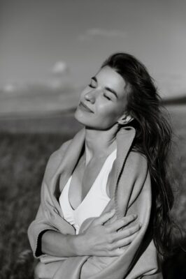 black and white photo of woman in a field, eyes closed, smile and in self-hug supporting herself