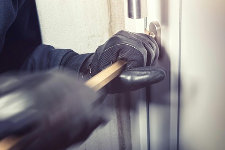 gloved hands using a crowbar to break a lock on a door and steal