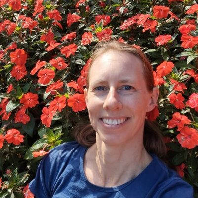 Author smiling from the bounty of her thoughts and emotions while surrounded by red flowers