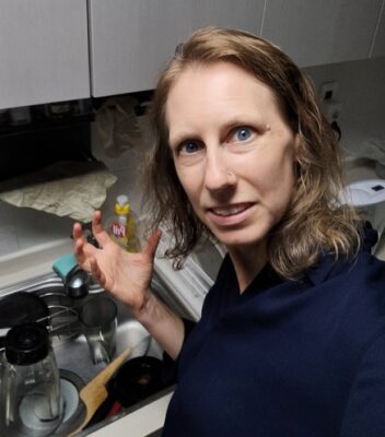 Author with a frustrated look and a pile of dirty dishes in the sink