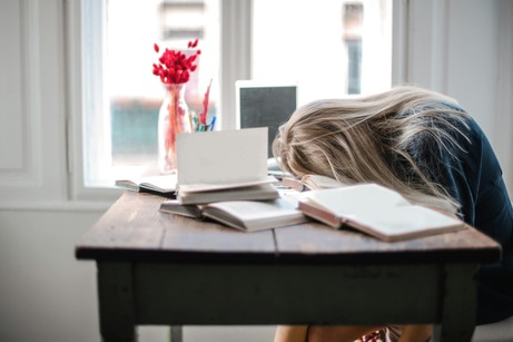 woman sitting at a desk with head, face down on top of books in burnout