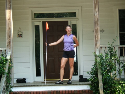 Author at the end of her ride posed  on the porch with the bike trailer's flag, proud and grateful