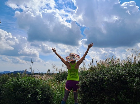 Woman with out stretched arms towards a green field and billowy clouded sky in joy